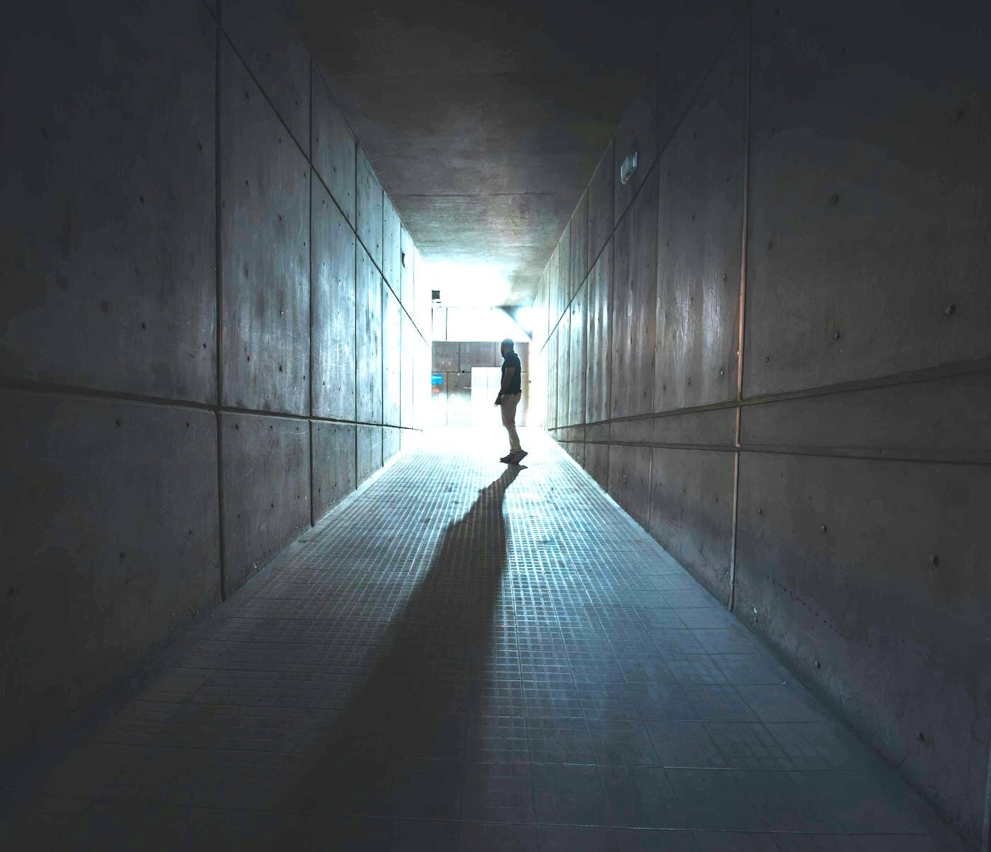 A lone figure at the far end of a long concrete underpass, throwing a shadow back down the passage